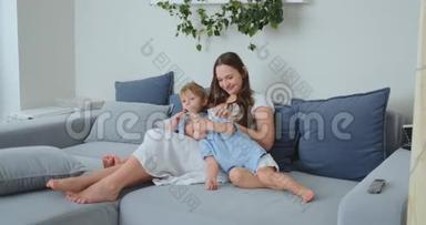 妈妈抱着两个小儿子在客厅的沙发上<strong>看电视</strong>.. 家庭<strong>看电视</strong>